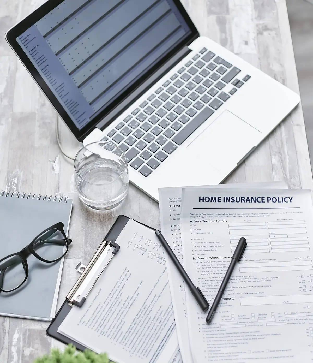 An insurance policy, a laptop, and office supplies spread on a desk.